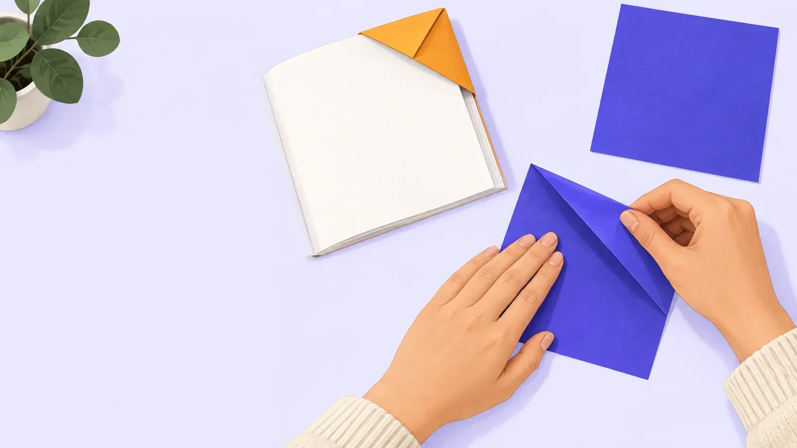 Hands press an indigo paper fold beside an orange corner bookmark on a blank book page