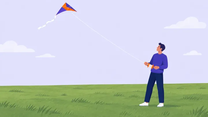 A person holds a winder connected to an orange and indigo delta kite above a wide open grassy field