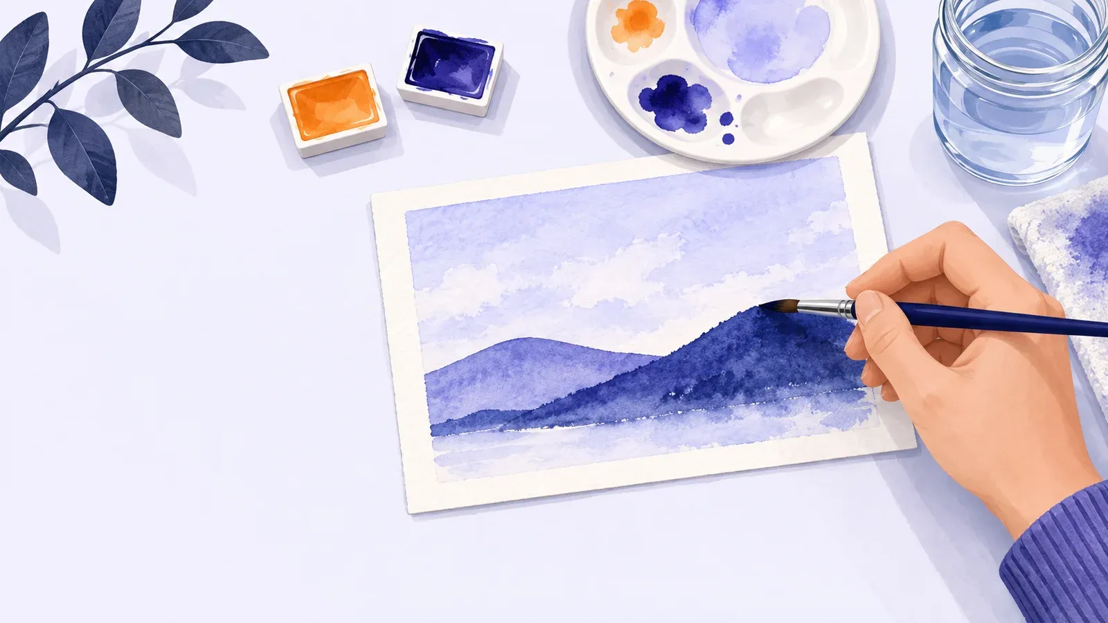 A hand paints an indigo hill on a small watercolor landscape beside paint pans and a water jar